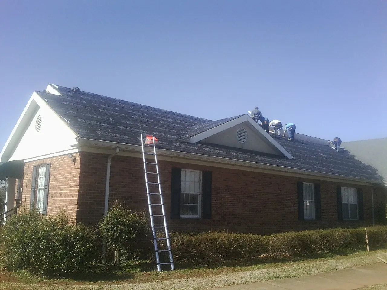 Crew tearing shingles off a brick ranch roof with a ladder set — Metal Roof Repair work by our crew in Wolfe City