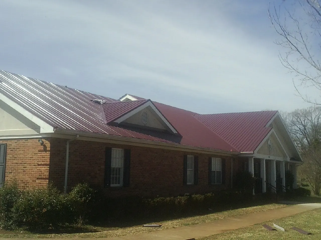 Red metal roof with gabled entries on a long brick building, from a Hail Damage Roof Repair job in Wolfe City