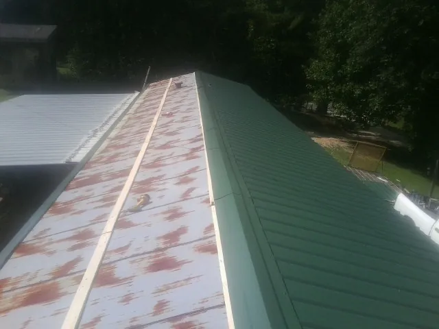 Old rusted panels beside newly installed green metal roofing — Wind Damage Roof Repair by Roofing Brothers in Wolfe City