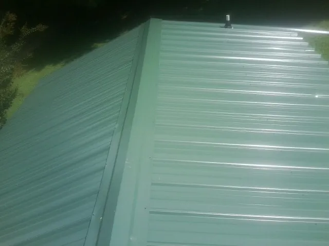 New green metal panels meeting at the ridge of a roof — Flat Roof Repair work by our crew in Wolfe City