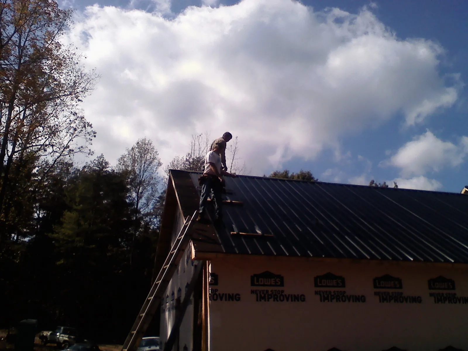 Roofer fastening dark metal panels high against a cloudy sky, from a Roof Inspection job in Wolfe City