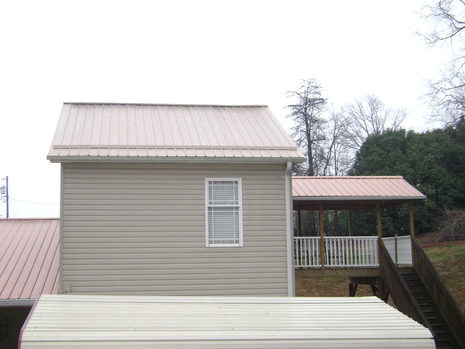 Tan metal roofs on a two story addition and attached porch, from a Roof Replacement job in Wolfe City